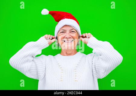 portrait and close up of old and mature woman smiling and having fun looking at the camera wearing christmas clothes with green background Stock Photo