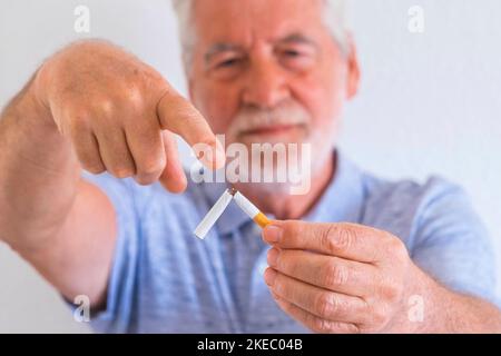 close up of mature man holding a cigar in his hands showing he can leave from the world of the smoke - stop smoking and the smoke kill concept and portait - senior with white wall at the background Stock Photo