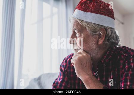 Portrait of one old and mature man sitting on the sofa of his home celebrating the Christmas Day alone and lonely and isolated from his family for the coronavirus Stock Photo