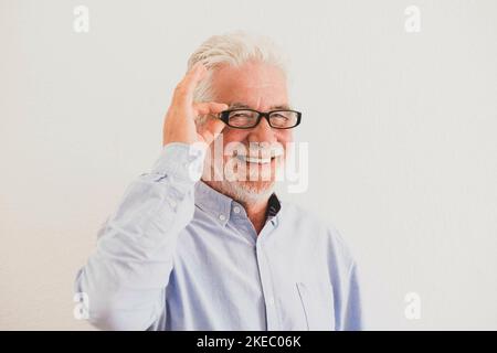 close up and potrait of mature man smiling and looking at the camera with a white wall at the background - active senior concept and lifestyle - intellectual and intelligence pensioner with glasses Stock Photo