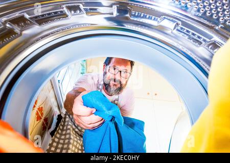 close up of mature man cleaning and washing the clothes at home in the washing machine in quarantine or lockdown - man helping in the home work Stock Photo