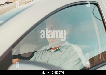Happy owner. Handsome bearded mature man sitting relaxed in his newly bought car looking out the window smiling joyfully. One old senior driving and having fun. Stock Photo