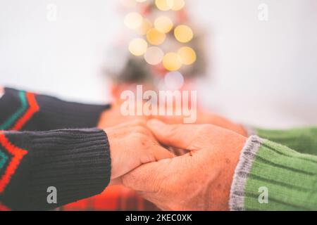 Senior couple in warm clothing holding each others hands at home. Loving old romantic heterosexual couple celebrating christmas festival together. Man and woman holding hands Stock Photo