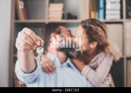 Focus on keys, held by excited young spouses homeowners. Happy married family couple celebrating moving in new house home, demonstrating keys, standing in apartment, real estate mortgage concept. Stock Photo