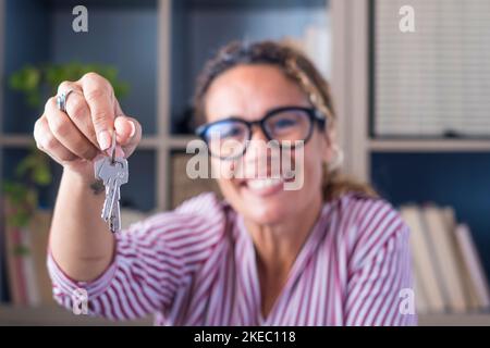 Happy woman showing keys of her new house or office. Portrait of smiling businesswoman holding key to her new apartment. Female tenant or renter moving or relocating with keys in her hand Stock Photo