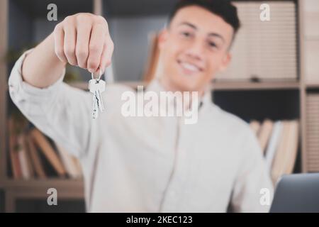 Focus on bunch of keys from house flat apartment in hand of smiling teenager. Blurred portrait of confident man professional realtor offering new dwelling real estate unit to potential buyer. Close up Stock Photo