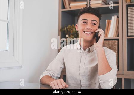 Smiling businessman wearing glasses talking on phone, sitting at desk with laptop, friendly manager consulting customer by phone, happy man chatting with friends distracted from work Stock Photo