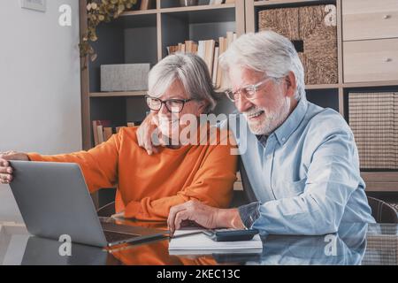 Elderly man and woman having fun using laptop at office. Smiling old husband and wife doing home finance online. Senior couple watching media content and enjoying at home Stock Photo