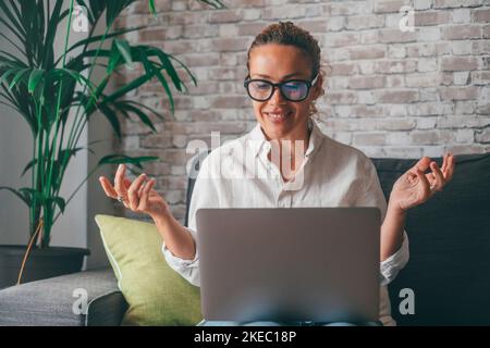 Concentrated young Caucasian woman in earphones sit at desk at home talk on video call on computer, focused female in headphones have virtual webcam conference or conversation on laptop with client Stock Photo