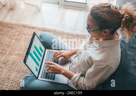 Close up rear view young woman using laptop and calculator, working on project, checking financial documents, sitting at table at home, looking at computer screen with diagrams, calculating bills Stock Photo