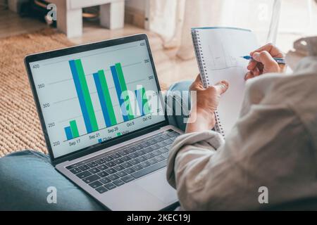 Close up rear view young woman using laptop and calculator, working on project, checking financial documents, sitting at table at home, looking at computer screen with diagrams, calculating bills Stock Photo
