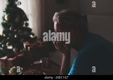 Portrait of one old and mature man sitting on the sofa of his home celebrating the Christmas Day alone and lonely and isolated from his family for the coronavirus Stock Photo