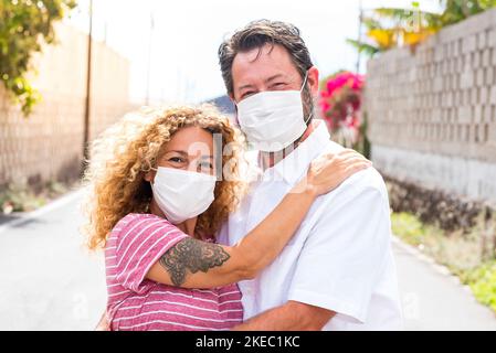 couple of happy people in love smiling and looking at the camera wearing medical and surgical mask on the face to prevent covid-19 or any type of disease or flu Stock Photo