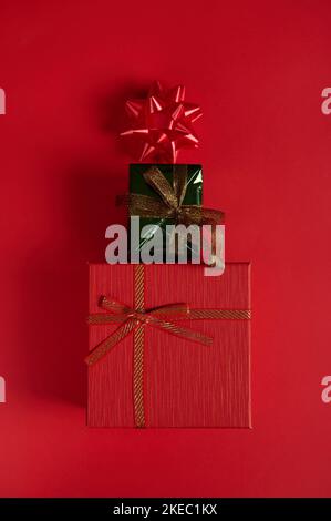 Flat lay. Vertical shot gift boxes laid out in shape of Christmas tree, decorated with bow on red background. Still life Stock Photo