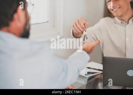 Crop close up of realtor give keys to man buyer or renter buying first home from agency. Real estate agent or broker congratulate male tenant with house or flat purchase. Ownership, rental concept. Stock Photo