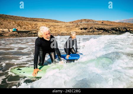 couple of seniors going surfing together - two mature people in the beach with surfboards and wetsuits looking at the sea entring in the water - learning surf Stock Photo