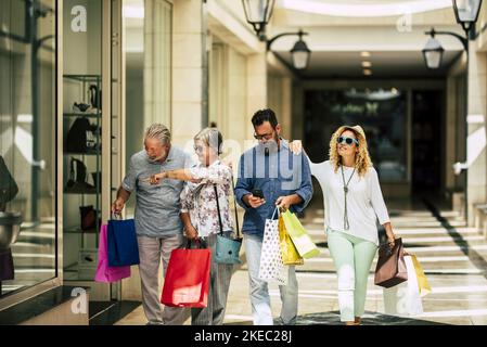 group of people going shopping together at the mall holding shopping bags - two seniors and couple of adults looking stores Stock Photo