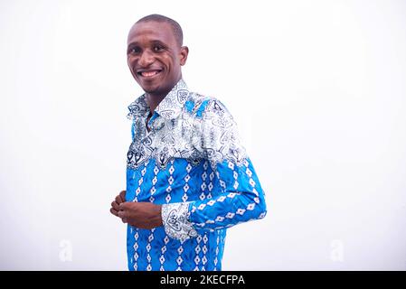 a young businessman standing on a white background staring at the button of his shirt and looking at the camera smiling Stock Photo
