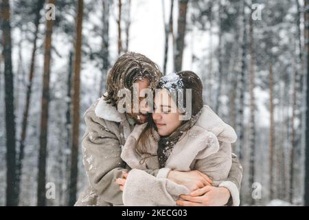 Love romantic young couple. Guy hugging kissing girl in snowy winter forest. Walking,having fun in trees, laughing. Stylish clothes,fur coat,jacket,wo Stock Photo