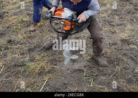 Shallow depth of field (selective focus) details with a man using a hand held earth hole drilling machine during a November tree planting on muddy soi Stock Photo