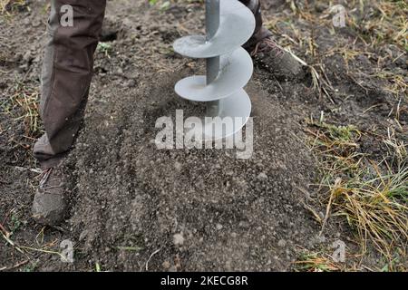 Shallow depth of field (selective focus) details with a man using a hand held earth hole drilling machine during a November tree planting on muddy soi Stock Photo