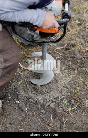 Shallow depth of field (selective focus) details with a man using a hand held earth hole drilling machine during a November tree planting on muddy soi Stock Photo