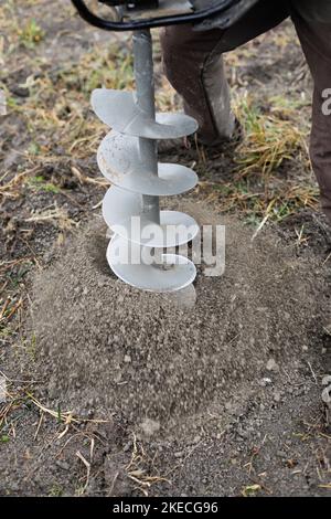 Shallow depth of field (selective focus) details with a man using a hand held earth hole drilling machine during a November tree planting on muddy soi Stock Photo