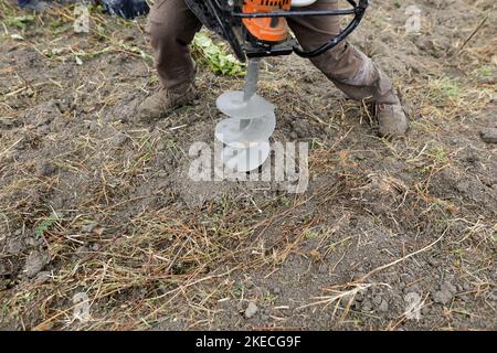 Shallow depth of field (selective focus) details with a man using a hand held earth hole drilling machine during a November tree planting on muddy soi Stock Photo