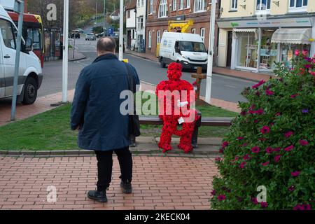 Chesham, Buckinghamshire. UK. 11 November, 2022. A man takes a photo of a striking Remembrance Day figure of man covered in red poppies sitting on a seat in Chesham next to the war memorial and holding a white dove. Credit: Maureen McLean/Alamy Live News Stock Photo