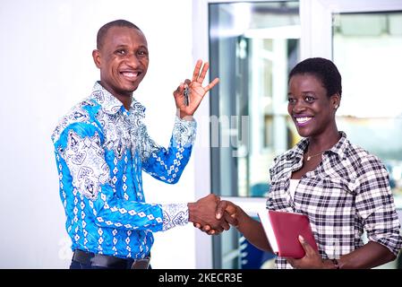 a businessman in a shirt standing in an office shaking hands with his partner and showing the key to his office smiling Stock Photo
