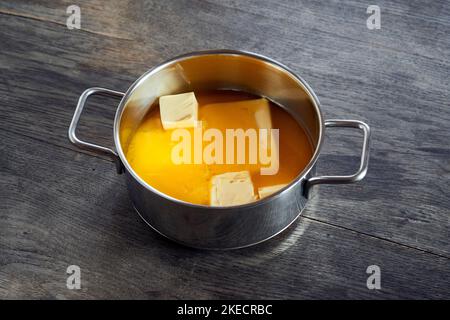 ayurvedic diet, steps to prepare homemade ghee from butter - organic sour cream butter in a stainless steel saucepan while melting, on a dark wooden table top. Stock Photo