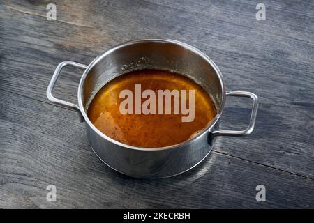 ayurvedic diet, steps to prepare homemade ghee from butter - melted sour cream butter in a stainless steel saucepan on a dark wooden table top, the ghee is clarified, sediments at the bottom of the saucepan Stock Photo