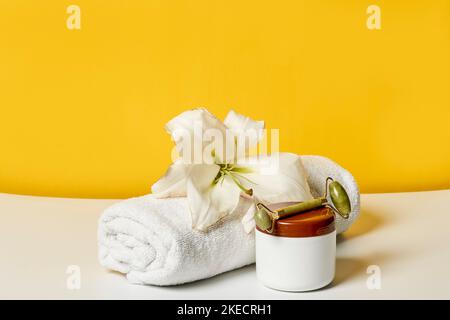 a white towel with a flower on it and a cup of hot tea sitting next to it in front of a yellow wall Stock Photo