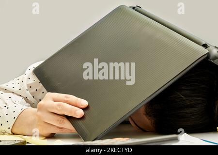 a person laying down with their head on top of an open laptop computer and papers scattered around them in the background Stock Photo