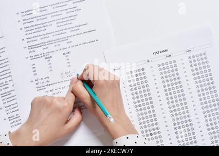 someone writing something on a piece of paper with a pen in their left hand and another person's right hand holding a pencil Stock Photo