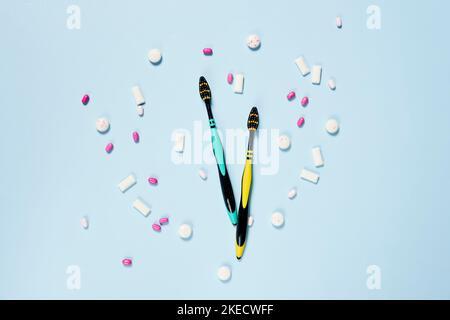 a clock made out of pills on a light blue background with white and pink candis scattered around the clock Stock Photo