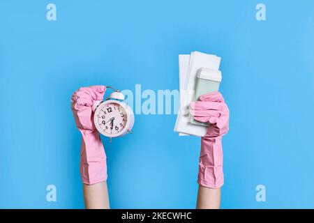 someone's hands holding an alarm clock and gloved in pink rubber gloves on a blue background with copy space Stock Photo