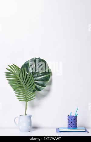 a plant next to a book on a white table with a blue cup and pencils in the foreground Stock Photo