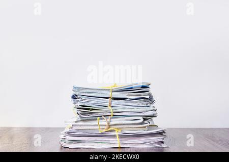 a stack of newspapers on a wooden table in front of a white wall, with yellow ribbon tied around the edges Stock Photo