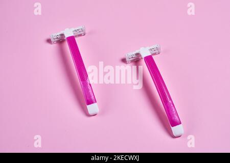 two toothbrushs on a pink background, one is white and the other is bright pink with an orange stripe Stock Photo