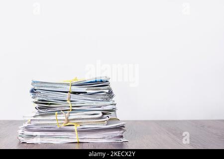 a stack of newspapers on a wooden table in front of a white wall, with yellow tape around the edges Stock Photo