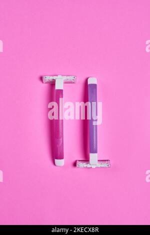 two toothbrushs on a pink background, one is white and the other is blue with a purple handle Stock Photo