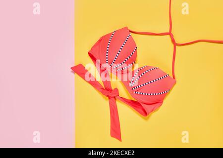 two pink and blue bikinis on a yellow background, with the one in black and white striped fabric tied around it Stock Photo