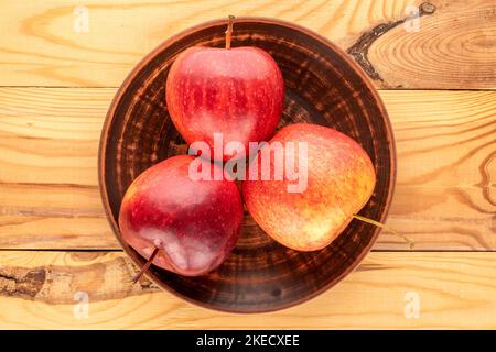 Three red juicy apples with a clay plate on a wooden table, macro, top view. Stock Photo
