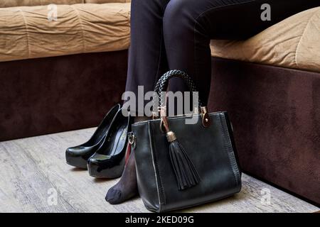 a woman sitting on a couch with her handbag and shoes in front of her, she is looking at the camera Stock Photo