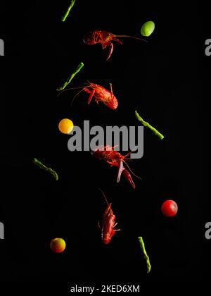 On a black background, red boiled crayfish, pieces of green asparagus and multi-colored cherry tomatoes in a frozen flight. Culinary blog, menu design Stock Photo