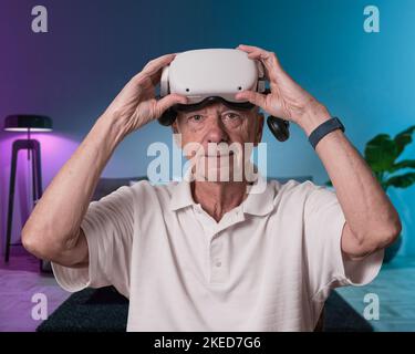 Senior adult man removing his virtual reality headset after exploring a scene in the metaverse Stock Photo