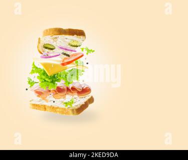 Creative culinary composition. Appetizing American sandwich with organic meat and cheese, fresh vegetables in a frozen flight on a beige background. R Stock Photo