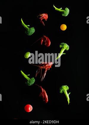 Stylish culinary composition. On a simple black background, a bright assortment of boiled crayfish, broccoli, cherry tomatoes in frozen flight. Vitami Stock Photo