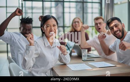 group of different business people celebrating victory while sitting at table in modern office Stock Photo